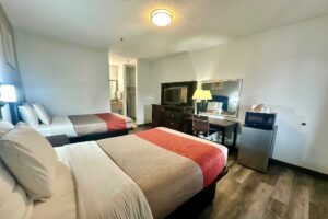 2 double beds, night stand, wall light, art image, wooden drawer unit with TV, desk with lamp and chair, fridge with microwave, laminate flooring, alcove with vanity unit, rail with towels, hanging rail with hangers