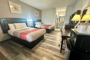 2 double beds, night stand with telephone, art images, fridge with microwave, desk with lamp and chair, mirror, wooden unit with TV, laminate flooring, alcove with vanity unit, mirror, hairdryer and rail with towels, tiled flooring