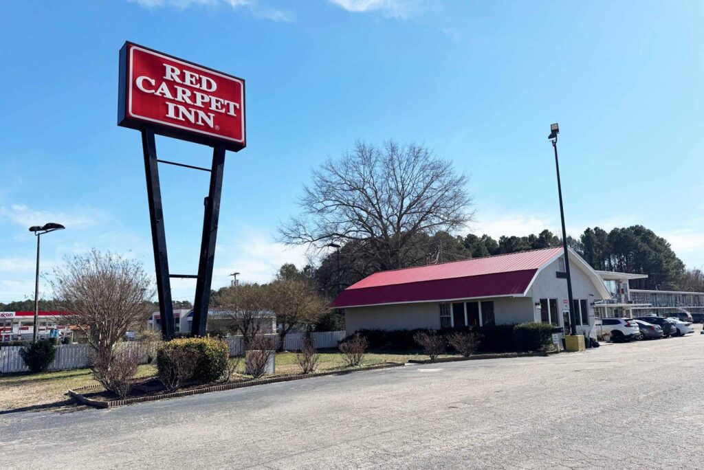 Battleboro-100 Hotel entrance, one story building, brand signage, grassy area with small bushes, parking spaces