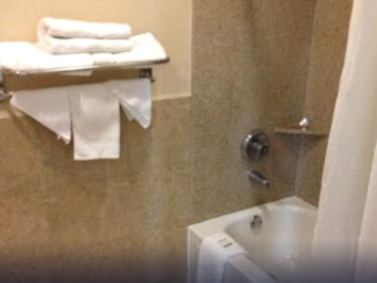 shower tub with shower curtain, bath mat, bathroom amenities and towels on a wall mounted towel rack