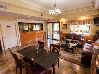 Lobby with front desk check in, sofa, love seat, floor rug, cofee table, breakfast area with table and chairs and wall mounted TV in the corner