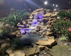 Exterior Fountain featuring flowers and bushes with water cascading over rocks