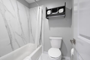 Shower tub with shower curtain and bathmat, toilet, unit with towels, tiled flooring
