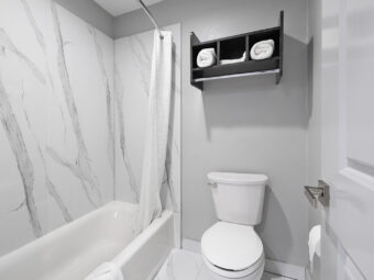 Shower tub with shower curtain and bathmat, toilet, unit with towels, tiled flooring