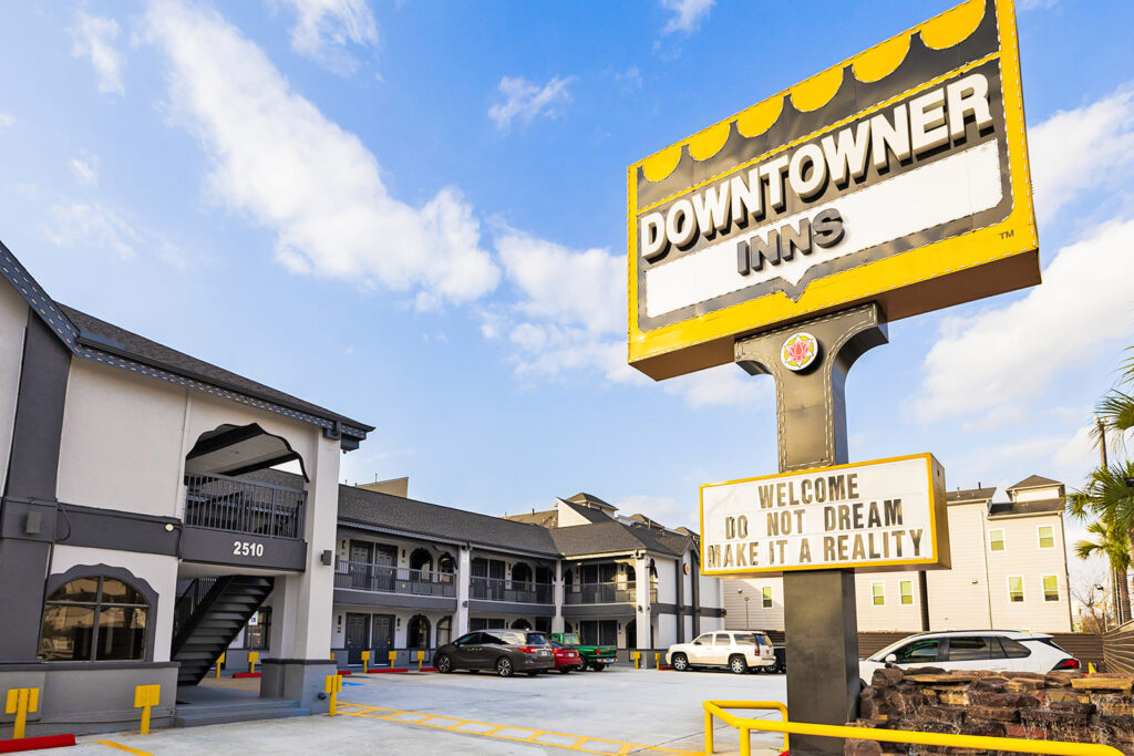 DTXHO Exterior 3 Brand signage, two story building with covered walkways, stairs and exterior guest room entrances, parking spaces