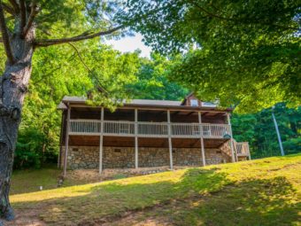 Cabin exterior showing wooden decking with wooden fencing, exterior wooden steps, trees, grassy area and landscaping