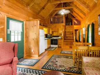 Cabin Front door, fridge, dishwasher, stove, microwave, microwave, table and chairs, sofa, wooden stairs leading to bedroom, side hallway with rear door and windows, wooden floor with rugs