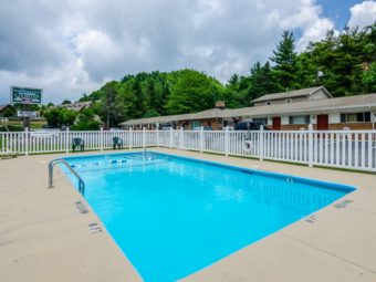 outdoor pool with concrete deck and patio furniture, white safety fencing and life saver, motel signage, motel rooms and parking area