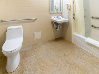 Grab rail, toilet, sink, hairdryer, mirror, showertub with shower curtain, bath mat and grab rails, tiled flooring