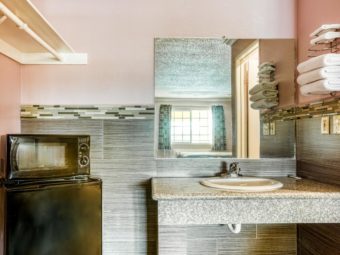 Vanity unit with sink, wall mounted towel rack with towels, wall mounted mirror, hanging rail with overhead shelf, fridge and microwave