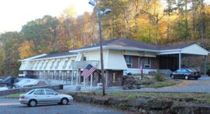 Hotel exterior with parking area and overlooked by tall trees