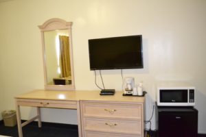 Desk, Wall mounted mirror, wall mounted flat screen tv, wooden drawer unit with coffee maker, fridge, microwave, carpet flooring