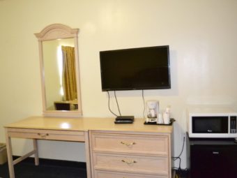 Desk, Wall mounted mirror, wall mounted flat screen tv, wooden drawer unit with coffee maker, fridge, microwave, carpet flooring