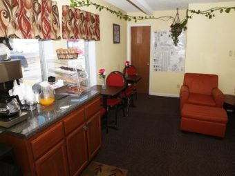 Breakfast display counter with coffee machine, juice pitcher, display case with breakfast pastries, tables with chairs, wall mounted local map, small occasion table, easy chair with foot stool extension and carpet flooring