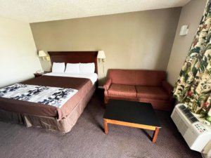 king bed, night stand with telephone, wall bedside lights, sofa, occasional table, carpet flooring