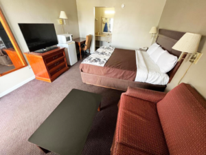 Full length mirror, wooden drawer unit with TV, fridge, microwave, desk with chair, wall light, king bed, night stand with telephone, wall bedside lights, sofa, occasional table, alcove with vanity unit, mirror and ironing board, carpet flooring