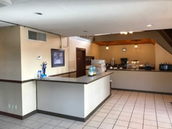 Breakfast counter displays with milk and juice pitchers, cereal dispensers, microwave, toaster, display case with breakfast patries and tiled flooring