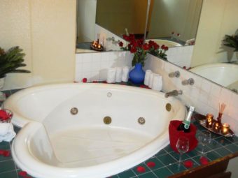 Jacuzzi, mirrored walls, tiled surround, bottle of champagne, wine glasses, vase with roses, candles and incense sticks on a tray, small green plant in vase