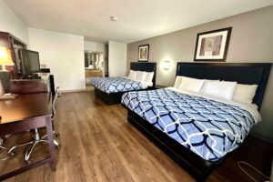 2 king beds, night stand wall light, art images, desk with lamp and chair, wooden unit with TV, laminate flooring, alcove with vanity unit, mirror, towel rail with towels, tiled flooring
