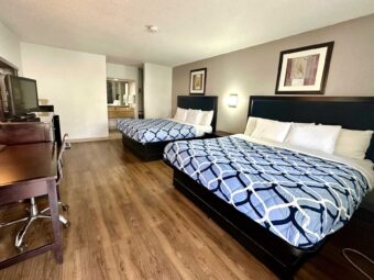 2 king beds, night stand wall light, art images, desk with lamp and chair, wooden unit with TV, laminate flooring, alcove with vanity unit, mirror, towel rail with towels, tiled flooring