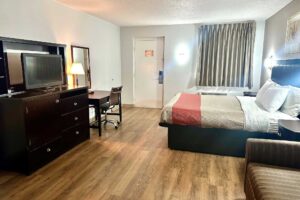 king bed, night stands, art image, wall light, sofa, wooden drawer unit with TV, desk with chair, lam, telephone and chair, mirror, laminate flooring