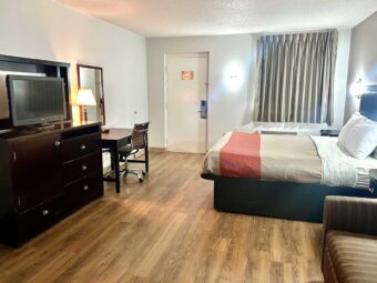 king bed, night stands, art image, wall light, sofa, wooden drawer unit with TV, desk with chair, lam, telephone and chair, mirror, laminate flooring
