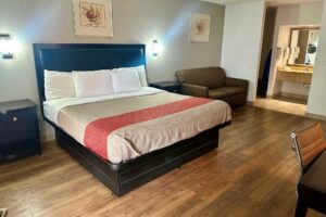 King bed, night stands, wall lights, art images, sofa, desk with chair, laminate flooring, alcove with vanity unit with mirror, towel rail with towels, tiled flooring