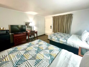 Two double beds, night stand, fridge with microwave, drawer unit with TV, desk with lamp and telephone and chair, mirror, laminate flooring