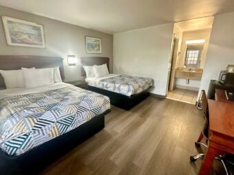 Two double beds, art images, wall light, night stand, desk with chair and telephone, drawer unit with TV, fridge with microwave, laminate flooring, alcove with vanity unit, hairdryer and mirror