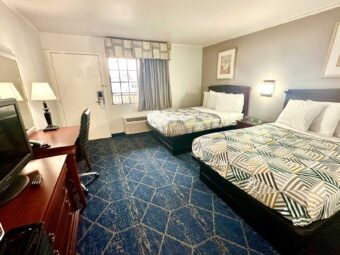 Two double beds, night stand, bedside light, art images, drawer unit with TV, fridge with microwave, desk with lamp, telephone and chair, mirror, carpet flooring