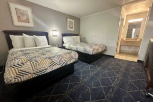 Two double beds, art images, night stand, carpet flooring, alcove with vanity unit, mirror and hair dryer