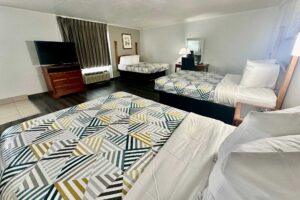 Three double beds, drawer unit with TV, art image, desk with chair and lamp, mirror, laminate flooring
