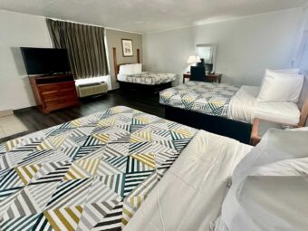Three double beds, drawer unit with TV, art image, desk with chair and lamp, mirror, laminate flooring