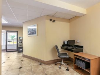 Wall mounted desk with computer screen and keyboard, office chair, wooden unit with printer, wall mounted art, atm machine and tiled flooring