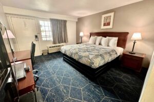 King bed, night stands with bedside lamps, unit with TV, desk with lamp and check, art image, carpet flooring