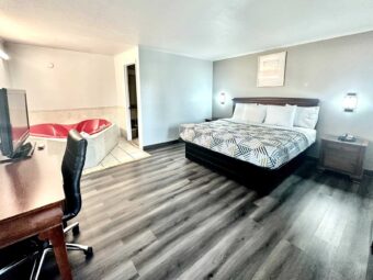 King bed, night stands with telephone, wall lights, art image, desk with chair and TV, laminate flooring, spa tub tiled flooring