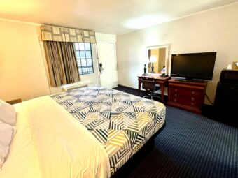 Queen bed, bedside light, desk with chair, lamp and telephone, wooden drawer unit with TV, fridge with microwave, carpet flooring