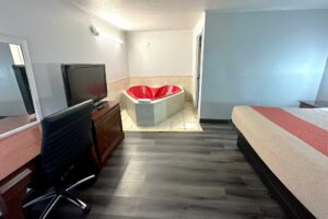 King bed, jetted tub, desk with chair, mirror, wooden drawer unit with TV, laminate and tiled flooring