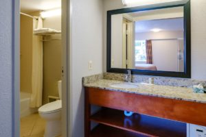 Vanity unit with sink and bathroom amenities, wall mounted mirror, doorway to bathroom with shower tub and toilet, tiled flooring