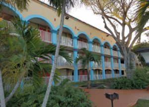 Three storey building showing exterior walkways, paved area, small bushes and palm trees