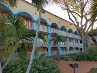 Three storey building showing exterior walkways, paved area, small bushes and palm trees