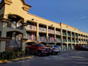 Three storey building with exterior walkways and stairs, small bushes and parking area