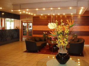 vase filled with flowers on a small glass table, two sofas, coffee table, side view of check in desk and tiled flooring