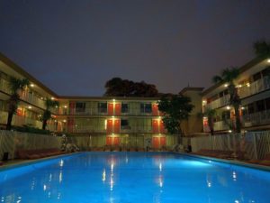 Night time shot of outdoor pool surrounded by three storey hotel building
