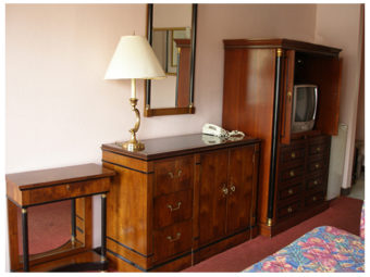 Small desk, wooden unit with drawers, cupnoard and table lamp, wooden tv console with tv, wall mounted mirror, edge of double beds and carpet flooring