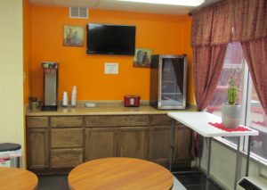 Breakfast counter display with small fridge, wall mounted art, wall mounted flat screen tv, small tables and tiled flooring