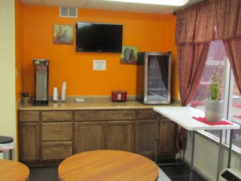 Breakfast counter display with small fridge, wall mounted art, wall mounted flat screen tv, small tables and tiled flooring