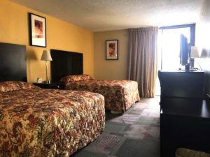 Two queen beds, night stand with bedside lamp, art images, wooden drawer unit with tv and carpet flooring