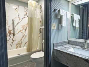 vanity unit, mirror, towel rail with towels, doorway to bathroom, toilet, shower tub with shower curtain, tiled flooring