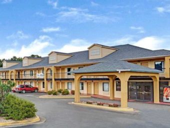 Hotel entrance with canopy, vending machine, small bushes and flowering shrubs, two storey building and parking spaces